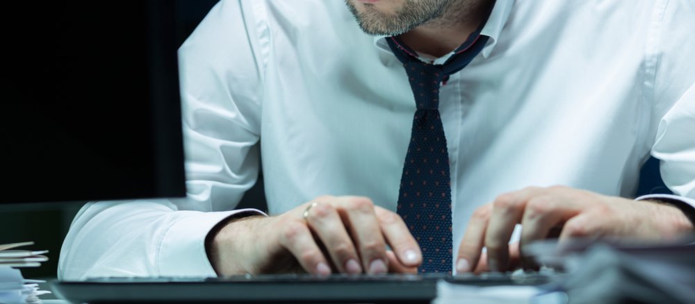 Hände eines Mannes mit Hemd und Krawatte tippen nachts auf Computertastatur.
