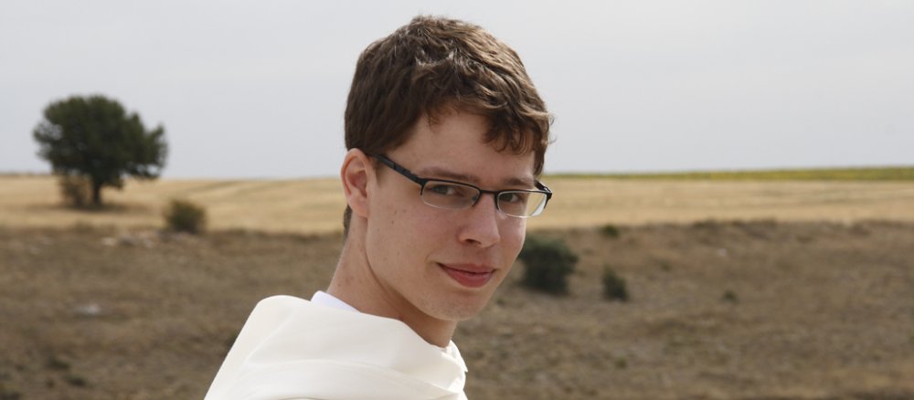 Ein junger Mönch im weißen Habit steeht vor einer kargen Landschaft.
