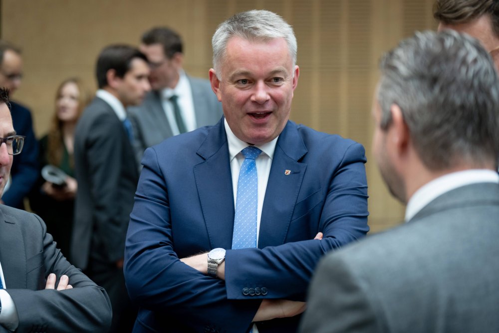 Ministerpräsident Gordon Schnieder steht mit verschränkten Armen in einer Menschenrunde und spricht.