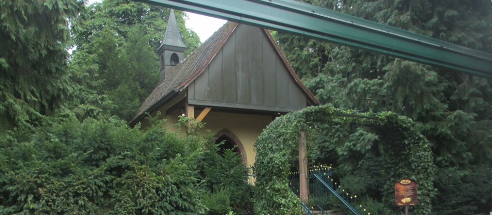 Menschen sitzen auf einer Holzbank vor einer Kapelle.