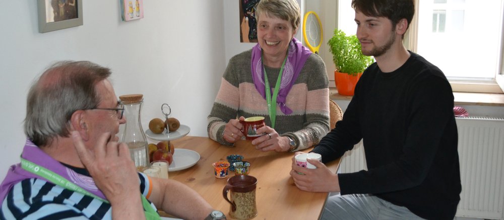 Drei Menschen sitzen in einer Küche an einem Tisch.