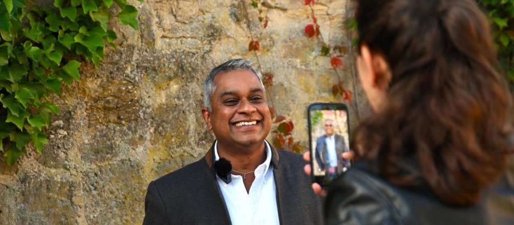 Der Mainzer Weihbischof Joshy Pottackal lächelt und blickt in eine Handykamera. Das Display ist sichtbar und zeigt Pottackal