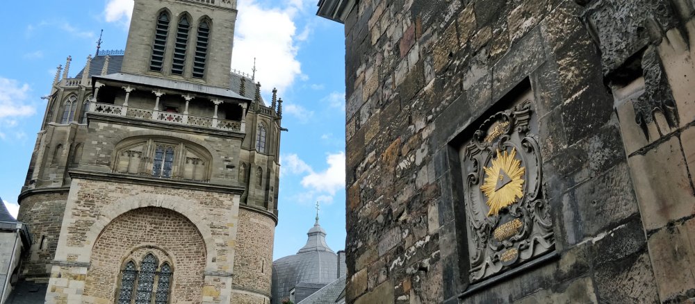 Links sieht man den Aachener Dom, rechts die Taufkapelle mit dem Symbol "Auge Gottes".