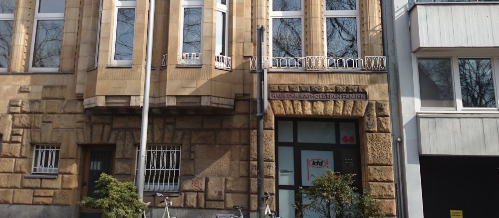 Der Eingang einer sandsteinfarbenen Stadtvilla neben einem modernen Wohnhaus.