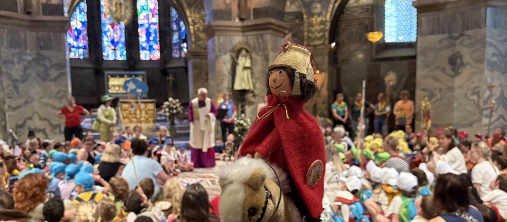 Pilgerstab-Puppe im Vordergrund, dahinter Domkapitular und Kinder beim Gottesdienst im Aachener Dom