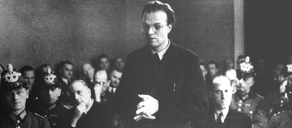 Schwarz-Weiß-Foto von 1945: Ein 37-jähriger Mann steht mit gefalteten Händen vor dem Volksgericht. Hinter ihm sitzt die Schutzpolizei.
