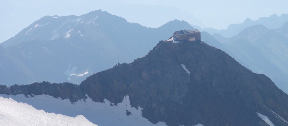 Blick auf ein Schneefeld in den Bergen mit einem Felsen, auf dem ein Haus gebaut ist