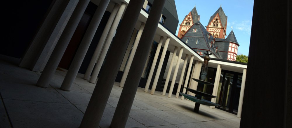 Das Bild zeigt den von Säulen umgebenen Innenhof des Diözesanen Zentrum in Limburg. Im Hintergrund heben sich die Türme des Doms ab.