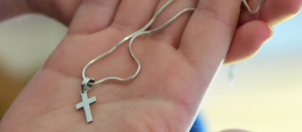 Eine Frau hält eine Kette mit einem Kreuzanhänger in der Hand.