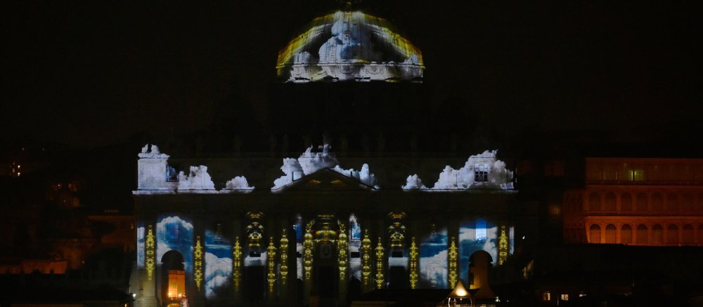 Eine Lichtinstallation zeigt Wolken auf der Fassade des Petersdoms.