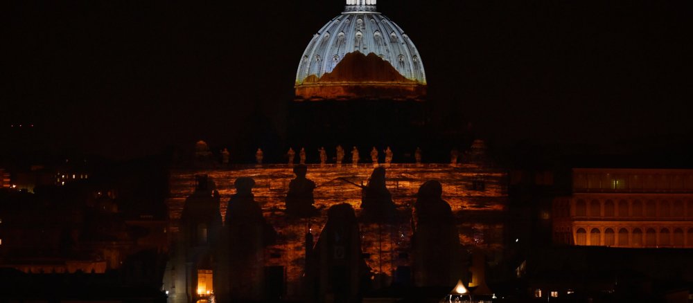 Eine Lichtinstallation zeigt Menschen in Booten auf der Fassade des Petersdoms.
