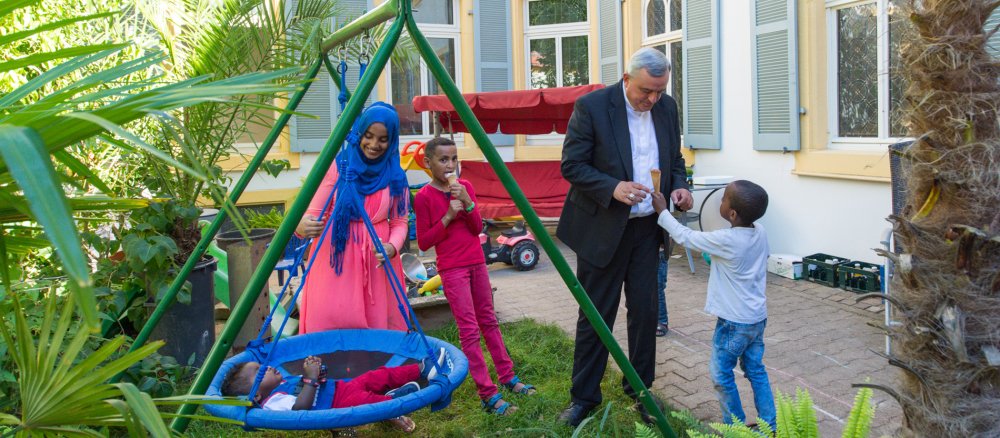 Karl-Heinz Wiesemann spielt im Garten des Vikarienhofs mit den Kindern der somalischen Flüchtlingsfamilie. Die Jungen essen Eis, die Mutter schaukelt einen ihrer Söhne in einer Schaukel.