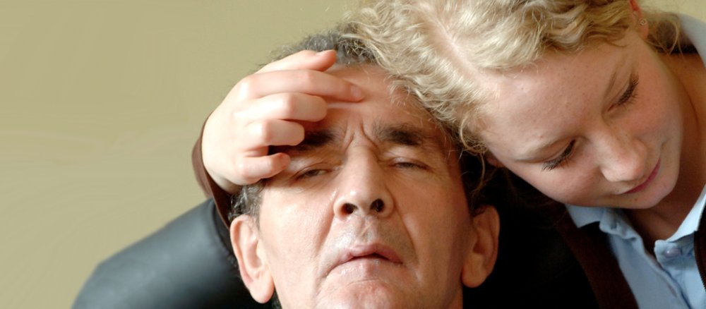 EineTochter nimmt zärtlich ihren Vater in die Arme, der nicht bei Bewusstsein ist.
