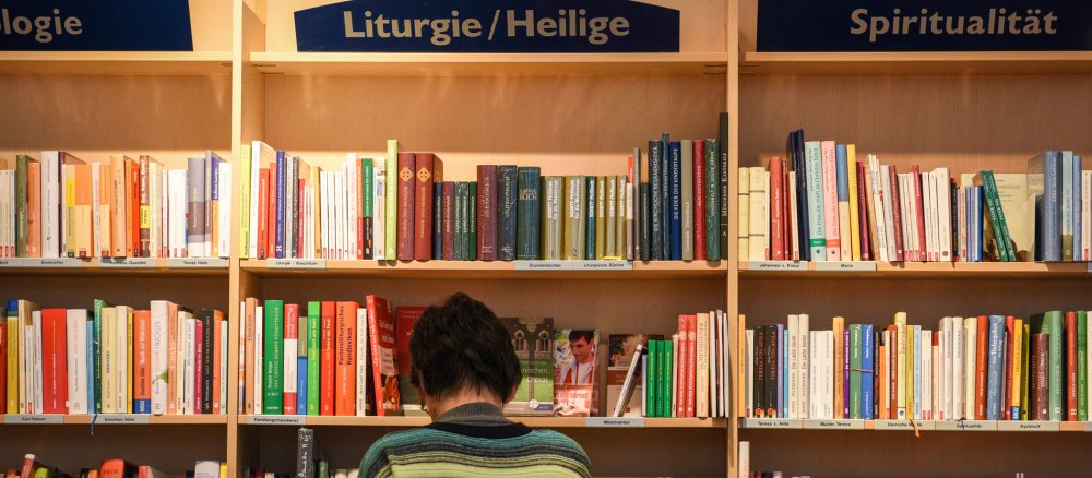Eine Frau steht vor Bücherregalen einer katholischen Buchhandlung.