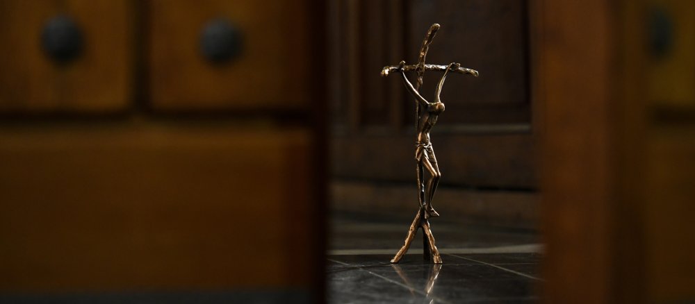 Blick durch eine leicht geöffnete Kirchentür auf ein Kruzifix