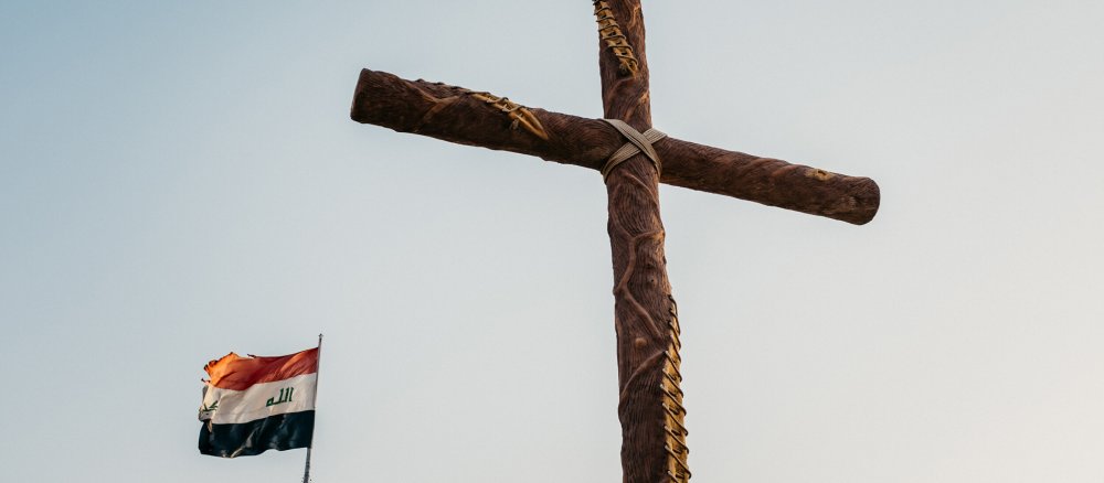 Ein großes Holzkreuz neben einer wehenden irakischen Nationalflagge.