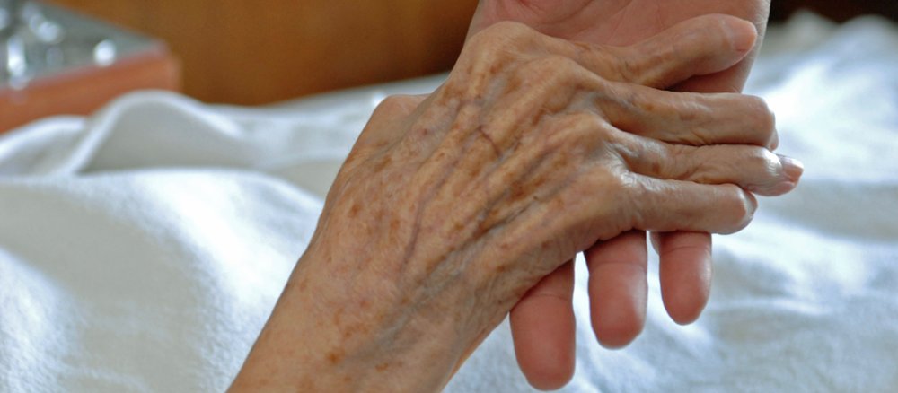 Ein Pfleger hält die Hand einer alten Frau.