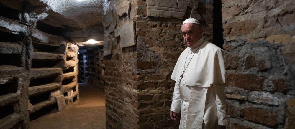 Papst Franziskus geht durch dunkle Katakomben-Gänge