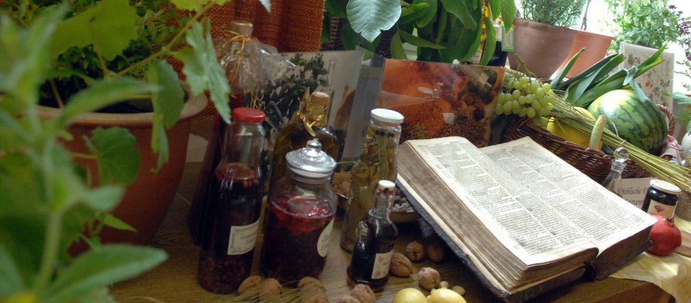 Eine 450 Jahre alte Hausbibel zwischen frischen Kräutern und Ölen auf einem Tisch.