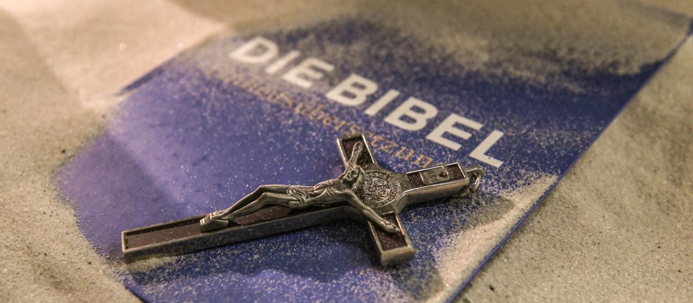 Eine Bibel und ein Kreuz liegen im Sand