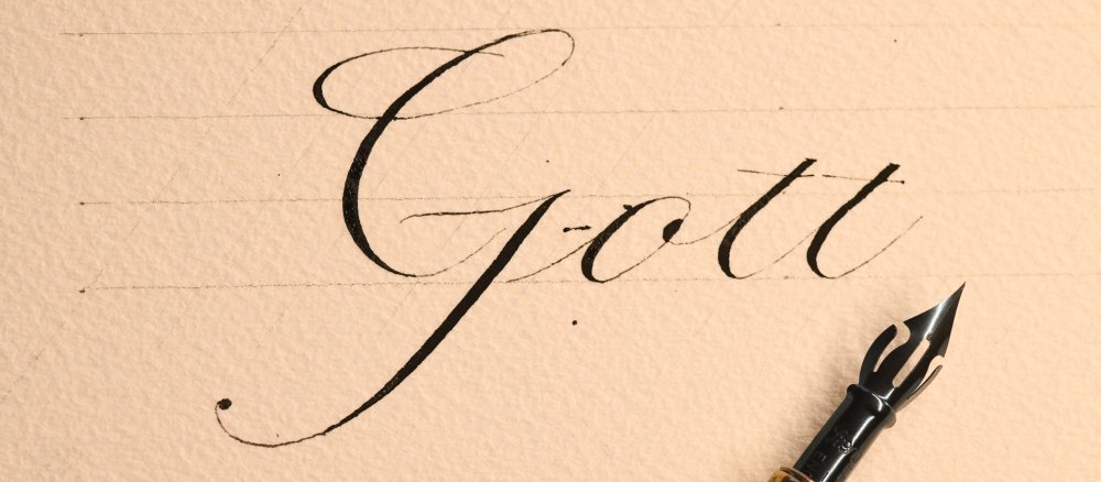 Auf einem Papier ist mit schwarzer Tusche das Wort Gott geschrieben