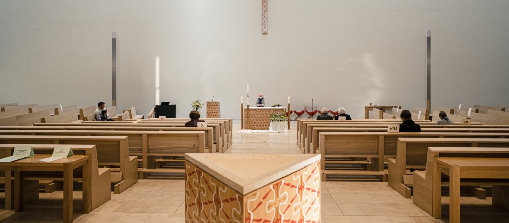 Gottesdienstbesucher sitzen mit großem Abstand zueinander in Kirchenbänken während einer Messe.