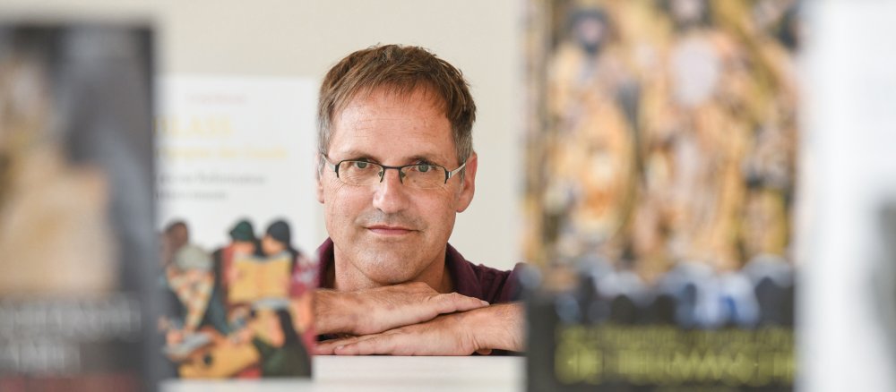 Georg Habenicht schaut zwischen einigen seiner Bücher in die Kamera