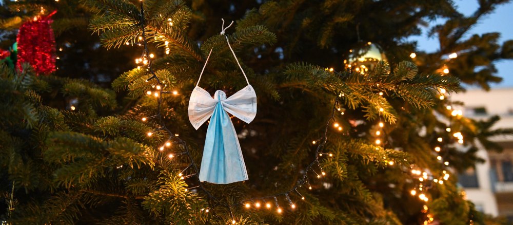 Ein Weihnachtsengel aus Atemschutzmasken gebastelt hängt mit Christbaumschmuck in einem Weihnachtsbaum.