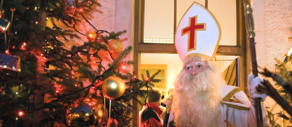 Nikolaus mit Mitra und Bischofsstab vor einer Haustür.