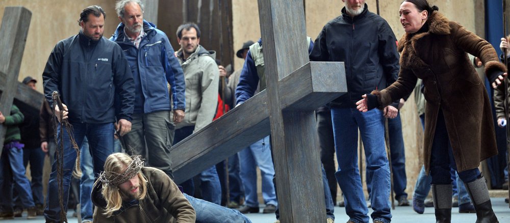 Ein Schauspieler mit einer Dornenkrone und einem Kreuz, daneben andere Schauspieler in Straßenkleidung