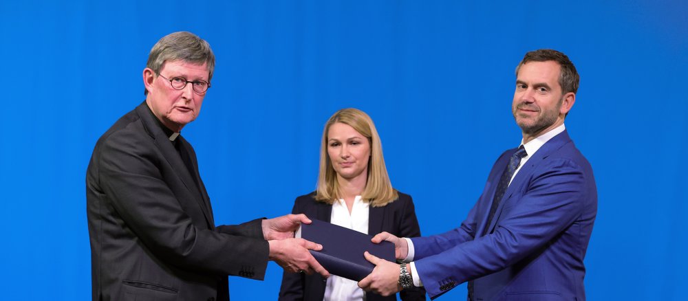 Rechtsanwalt Björn Gercke (r.) übergibt Kardinal Rainer Maria Woelki (l.) sein Gutachten, in der Mitte RA Kerstin Stirner