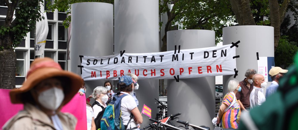 Eine Demonstration in Köln, im Hintergrund ein Plakat mit der Aufschrift "Solidarität mit den Missbrauchsopfern"