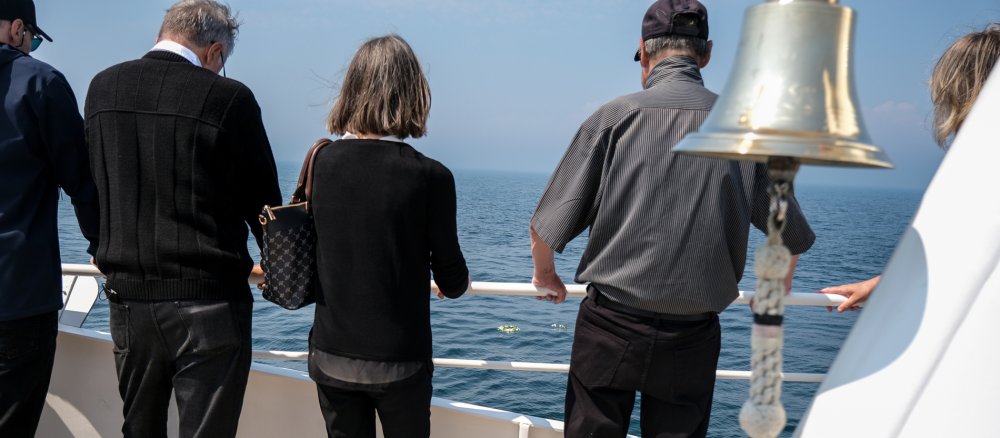 Trauergäste schauen nach einer Seebestattung auf die Blumen im Wasser