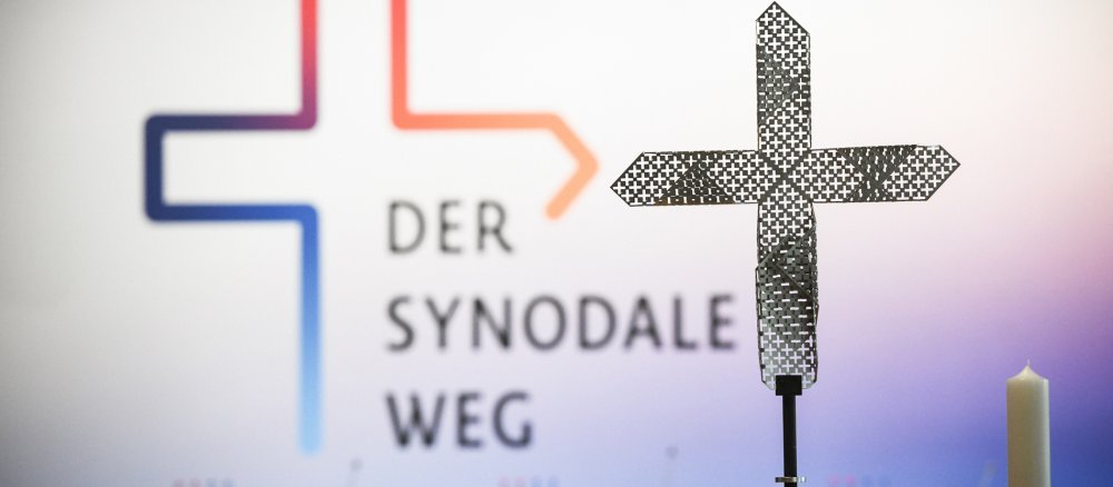 Das gelochte Metallkreuz und das Logo des Synodalen Weges