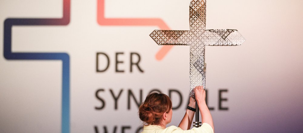 Metallkreuz und Logo des Synodalen Weges