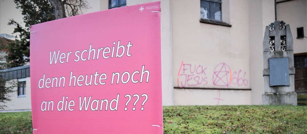 Rosa Schild mit der Aufschrift "Wer schreibt denn heute noch an die Wand??? Schreibt uns doch auf Insta!" vor Graffiti