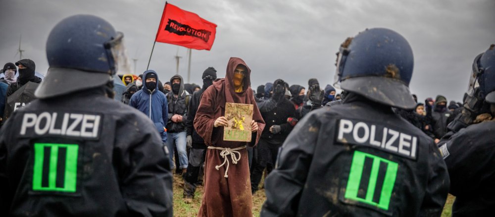 Ein Mann in Mönchskutte und Polizisten stehen sich bei der Räumung von Lützerath gegenüber