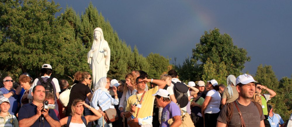 Pilger am Ort der angeblichen Marienerscheinung, in ihrer Mitte eine Marienstatue, am Himmel ein Regenbogen