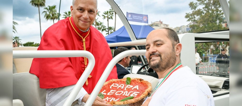 Ein Mann übergibt dem Papst eine Pizza, auf der mit Käse "Papa Leone XIV." steht.