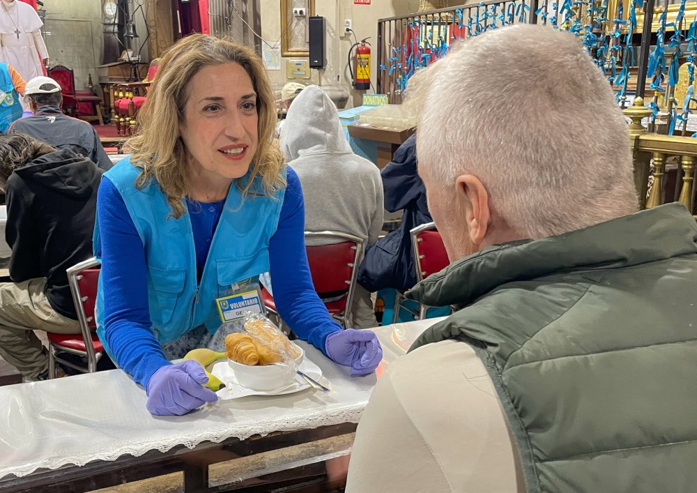 Gema Usón spricht in einer Kirche mit eine Bedürftigen. Vor ihr steht ein Teller mit Frühstück