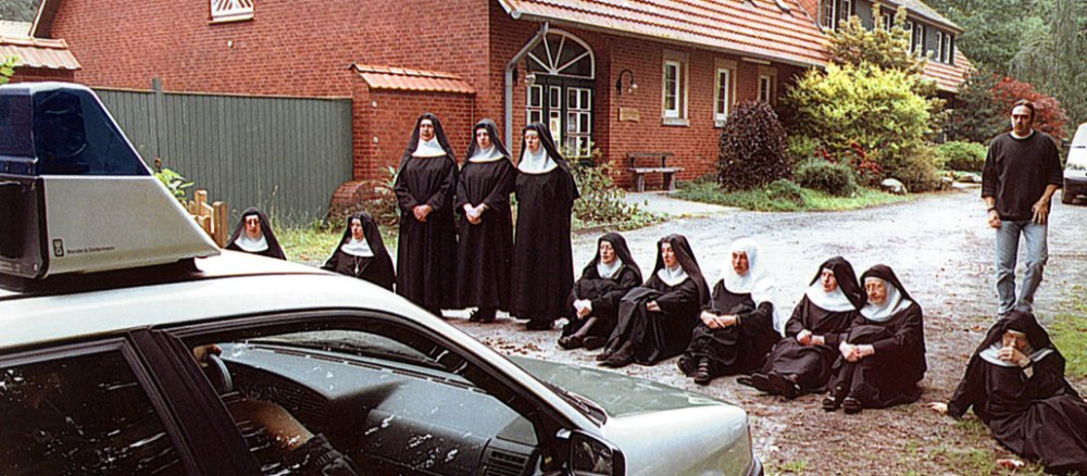 Elf Nonnen im Habit (sechs sitzend, drei stehend) demonstrieren vor einem Polizeiwagen.