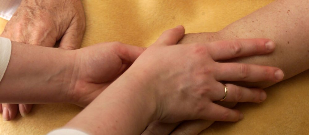 Ricam-Hospiz in Berlin. Eine Pflegerin hält die Hand einer Patientin.