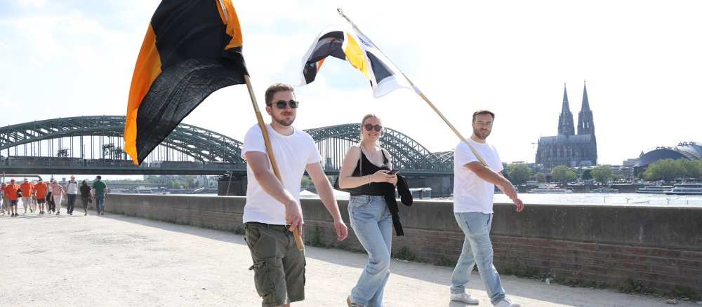 Junge Kolpinggeschwister mit Fahnen am Rheinufer gegenüber dem Kölner Dom