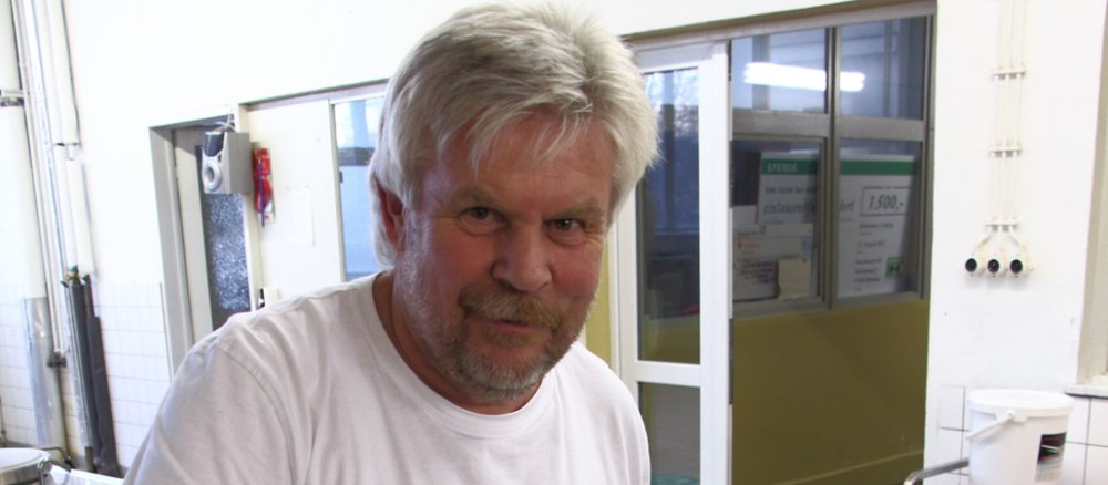 Ein Mann mit Bart rührt in einem etwa halbvollen Kochtopf mit Spinat.