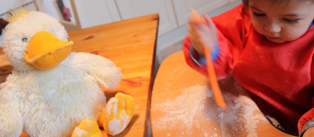 Kuschelente guckt einem Baby beim Spielen mit Mehl zu