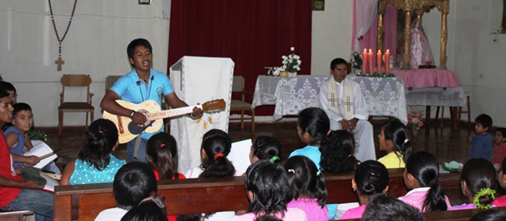 Die ersten Reihen der Kirche sind von Kinder bevölkert, die lauthals singen. Vor ihnen steht ein junger Mann mit einer Gitarre.