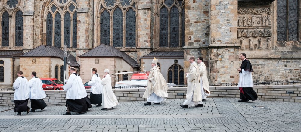 Vor einem Pontifikalamt gehen Zelebrant und Messdiener über den Domplatz in Paderborn.
