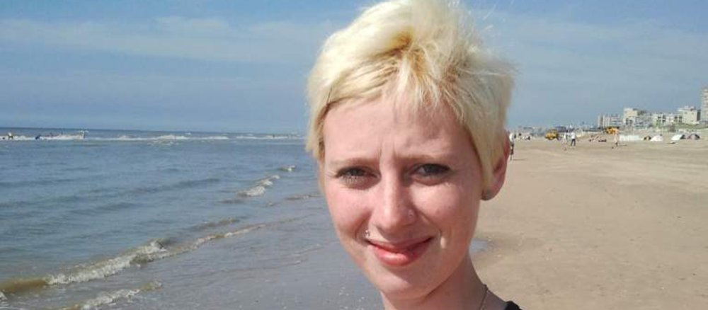 Hübsche junge Frau mit kurzen blonden Haaren steht an einem Strand.