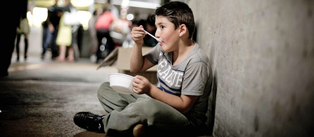 Kleiner Junge sitzt mit einer Schale Essen am Bahnhof