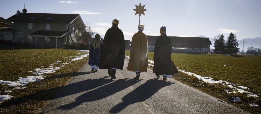 Vier Sternsinger gehen über einen Weg.